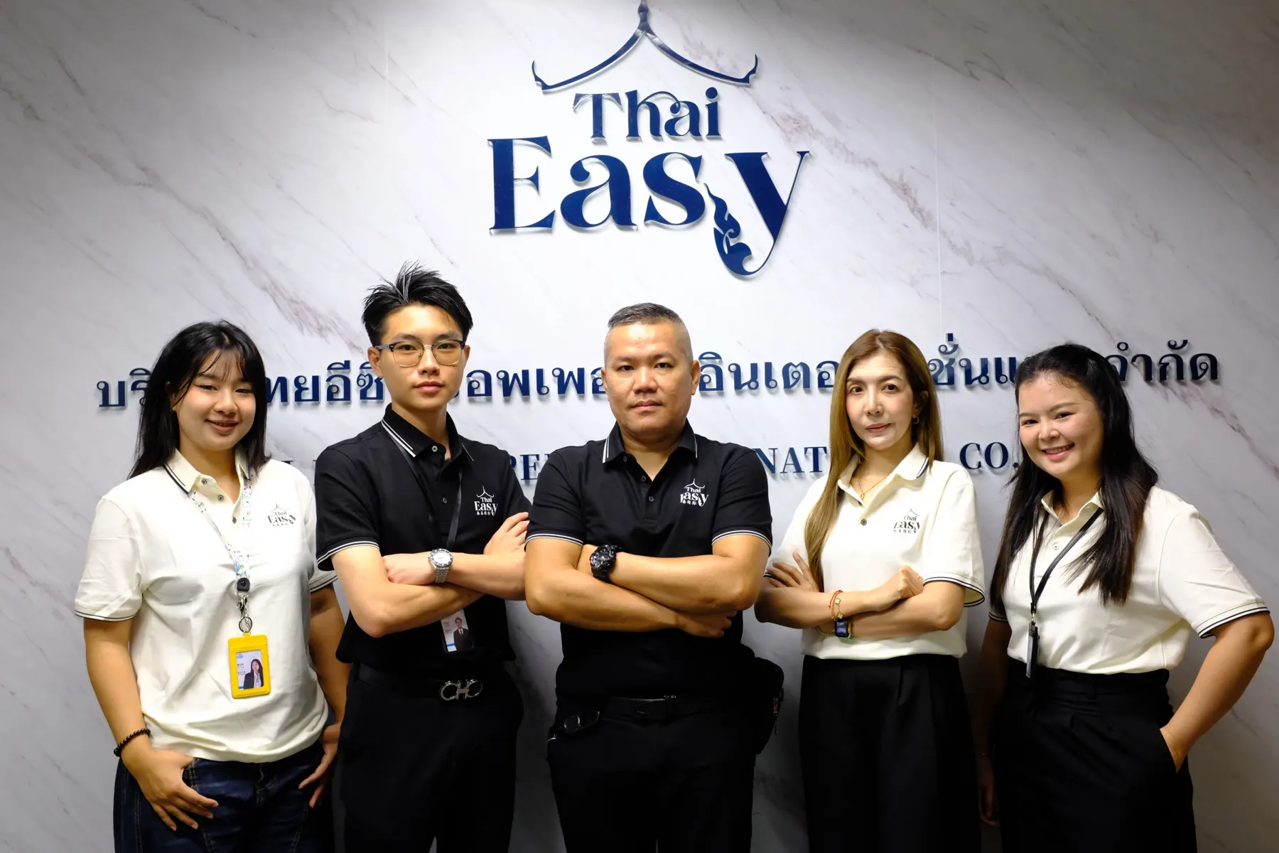 The Thai Easy team in front of the company logo wall